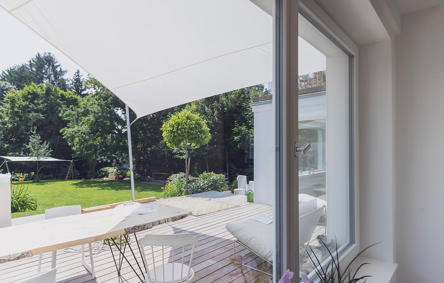 Luftige Sonnensegel für großzügige Terrassengestaltungen Blick aus dem Fenster in den sonnigen Garten - die Terrasse wird geschützt durch ein Sonnensegel