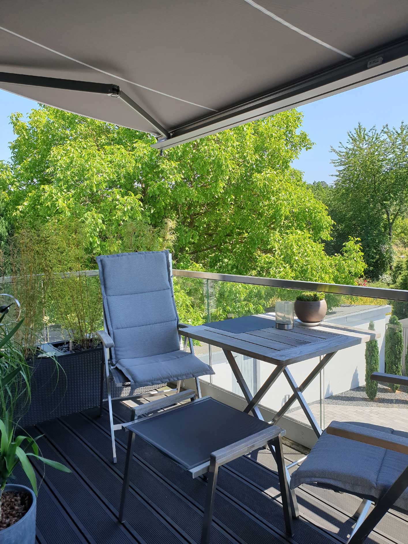 Handbetriebene Markise - Klassischer Sonnenschutz für jeden Haushalt Blick über schattigen Balkon auf den sonnigen Garten - geschützt durch eine Markise